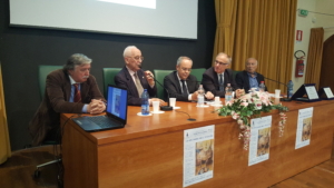 Alfredo Paglione parla dal palco della sala convegni, seduti vicino a lui altri relatori